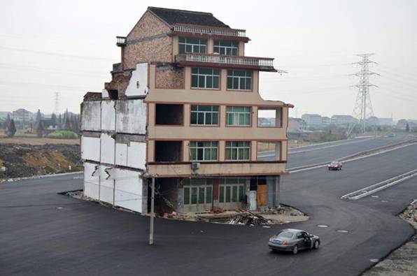 A car stops beside a house in the middle of a newly built road in Wenling, Zhejiang province, November 22, 2012. An elderly couple refused to sign an agreement to allow their house to be demolished. They say that compensation offered is not enough to cover rebuilding costs, according to local media. Their house is the only building left standing on a road which is paved through their village.